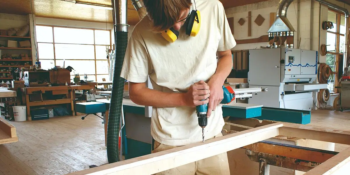 Ein Tischler arbeitet in seiner Werkstatt und bohrt mit einem Holzbohrer durch  Holz